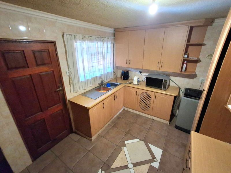 A functional kitchen featuring laminate cabinetry, tiled flooring, and a stainless steel sink, offering a dated aesthetic with potential for modern renovation.