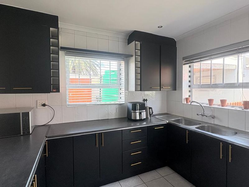 A functional kitchen featuring modern black cabinetry, contrasting white tiled backsplash, double stainless steel sink, and ample counter space with natural light.