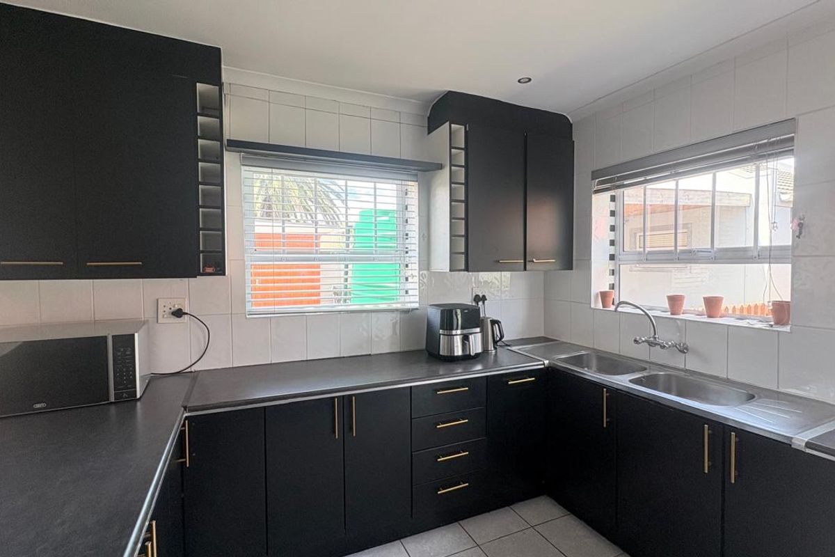 A functional kitchen featuring modern black cabinetry, contrasting white tiled backsplash, double stainless steel sink, and ample counter space with natural light.