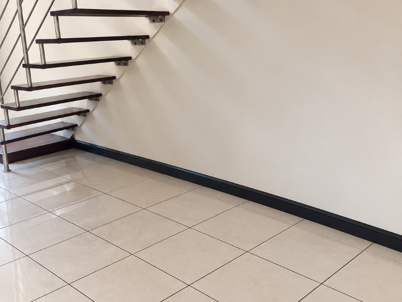 A modern hallway featuring a floating staircase with dark timber treads and a stainless steel balustrade, complemented by neutral ceramic floor tiles.