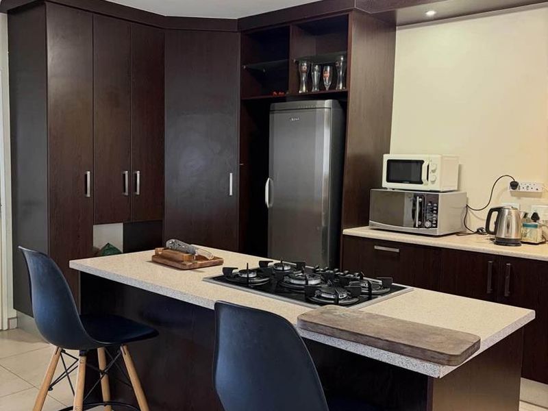 Modern kitchen featuring dark wood cabinetry, a central island with a built-in gas hob, stone countertops, and recessed ceiling lighting.
