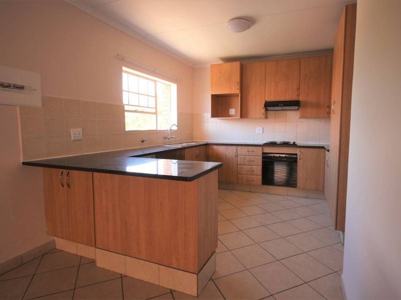 A functional kitchen featuring laminate cabinetry, granite countertops, built-in oven, gas hob, and tiled flooring, offering a clean and practical workspace.
