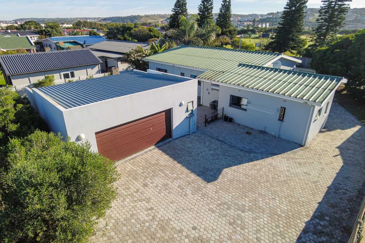 Aerial view of the property featuring a paved driveway, a detached garage, and a main house with a corrugated metal roof.