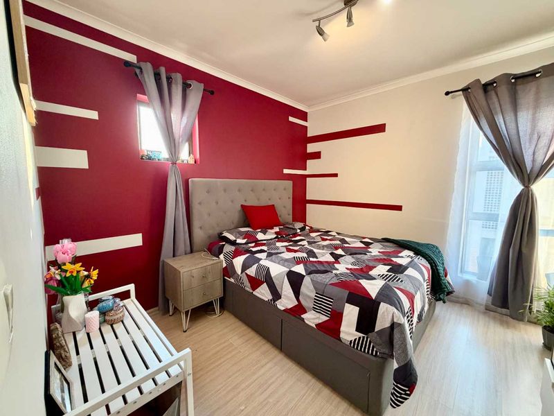 A well-lit bedroom featuring laminate flooring and a bold accent wall, providing a comfortable and functional sleeping space.