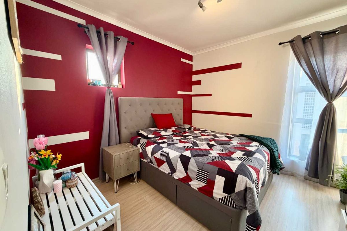 A well-lit bedroom featuring laminate flooring and a bold accent wall, providing a comfortable and functional sleeping space.