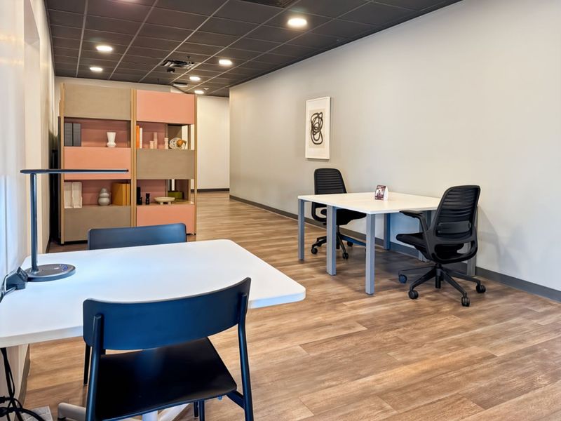 A modern, well-lit office space featuring wood-look flooring, a dark suspended ceiling with recessed lighting, and a functional built-in room divider.