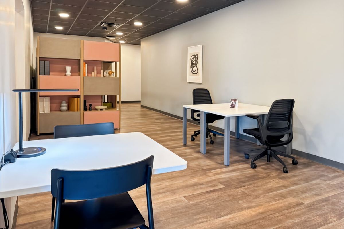 A modern, well-lit office space featuring wood-look flooring, a dark suspended ceiling with recessed lighting, and a functional built-in room divider.