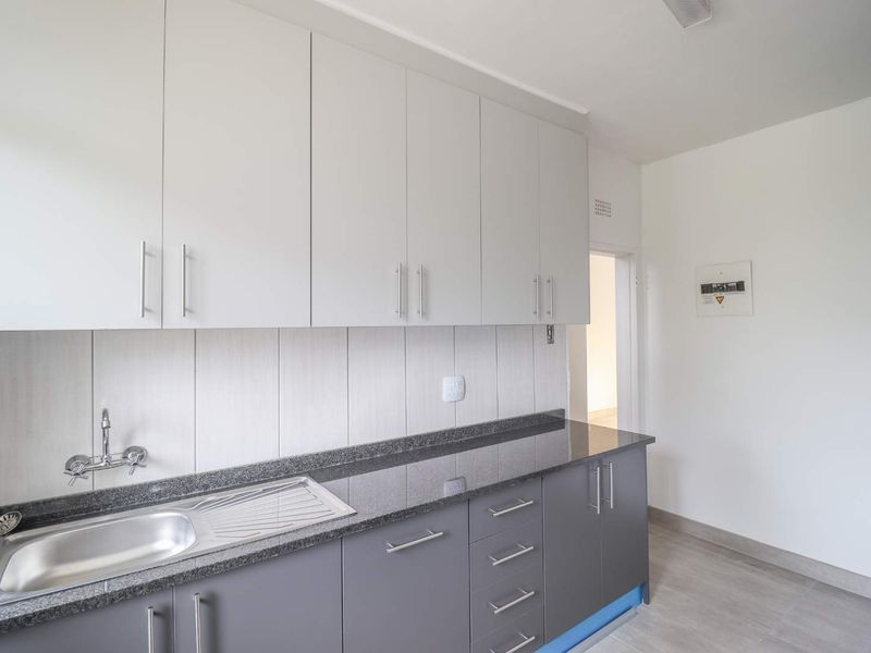 A clean, modern kitchen featuring grey lower cabinets, white upper cabinetry, granite countertops, and a stainless steel sink with a tiled backsplash.