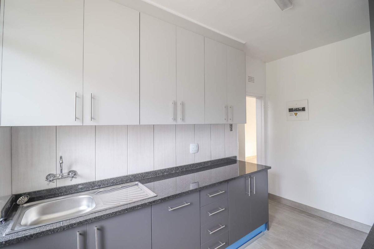 A clean, modern kitchen featuring grey lower cabinets, white upper cabinetry, granite countertops, and a stainless steel sink with a tiled backsplash.