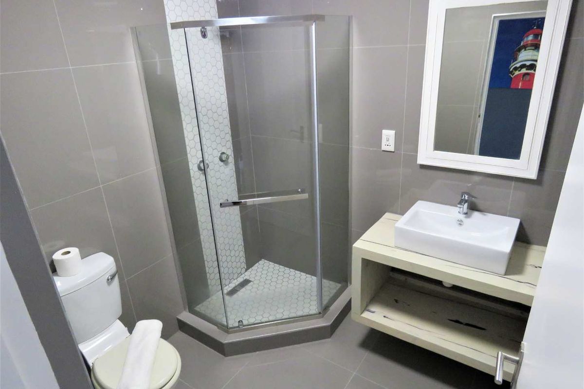 Modern bathroom featuring a corner glass shower enclosure with hexagonal tile accents, a vessel sink vanity, and neutral wall tiling.