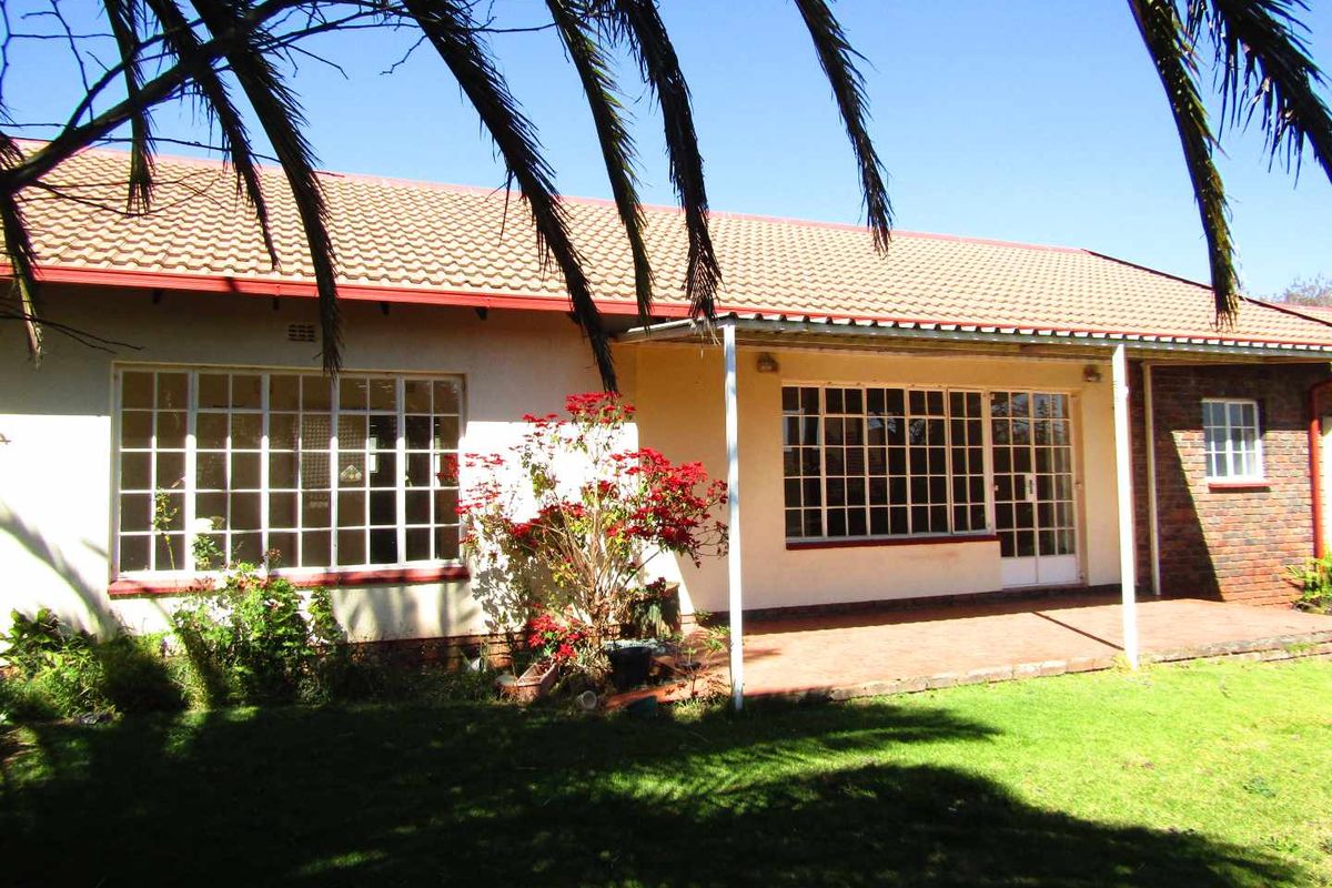 Rear view of the retirement village unit featuring a covered patio, tiled roof, and established garden area.