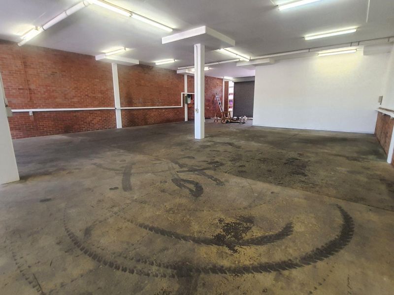 Spacious industrial utility area featuring exposed brick walls, concrete flooring, structural columns, and fluorescent lighting, suitable for workshop or storage use.
