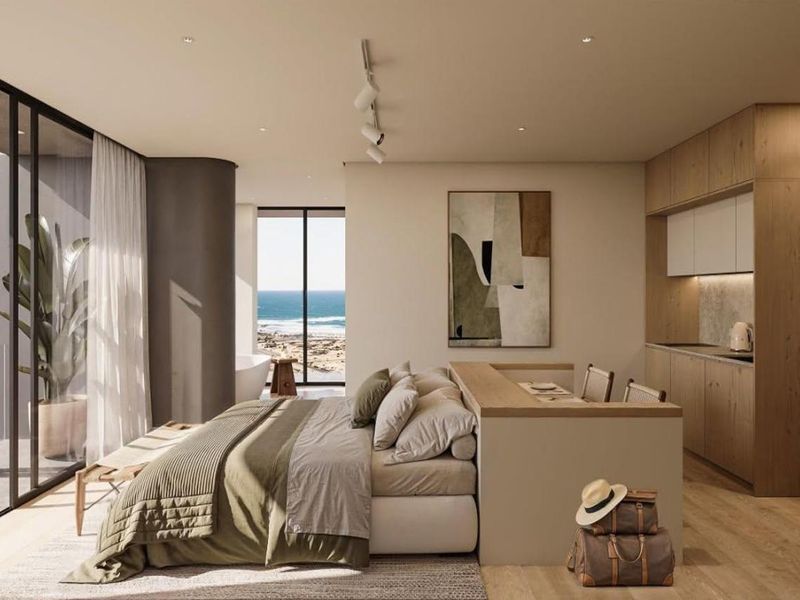 Modern open-plan hotel suite featuring a kitchenette, floor-to-ceiling windows with ocean views, and high-end contemporary finishes throughout.