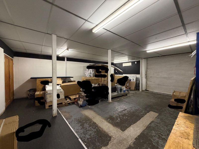 Spacious garage area featuring a roller shutter door, painted concrete flooring, and functional overhead fluorescent lighting, suitable for storage or workshop use.