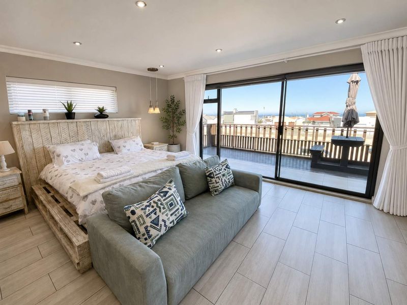 Spacious bedroom featuring modern tiled flooring, recessed lighting, and large sliding glass doors opening onto a private balcony with coastal views.