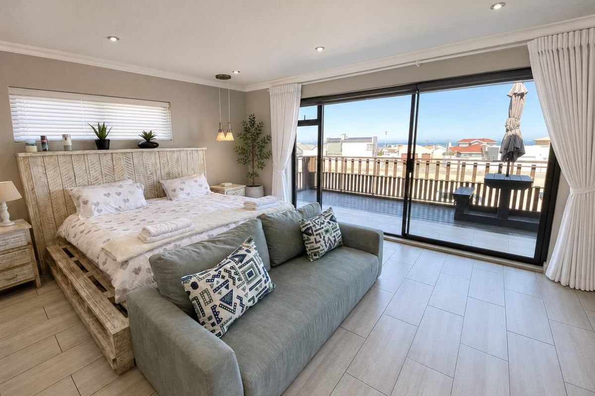 Spacious bedroom featuring modern tiled flooring, recessed lighting, and large sliding glass doors opening onto a private balcony with coastal views.