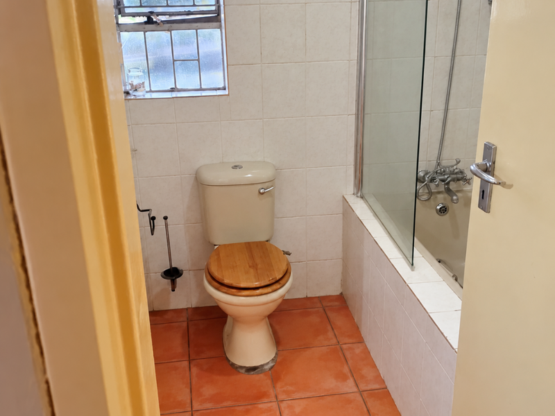 A functional bathroom featuring a shower-over-bath combination, tiled walls and flooring, and a window with security bars.