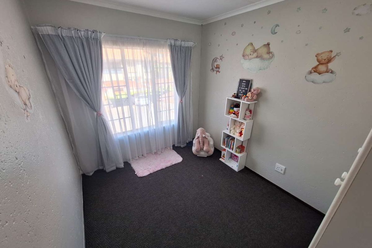 A bedroom featuring dark carpeting, neutral walls, and a window with curtains, currently styled as a nursery.