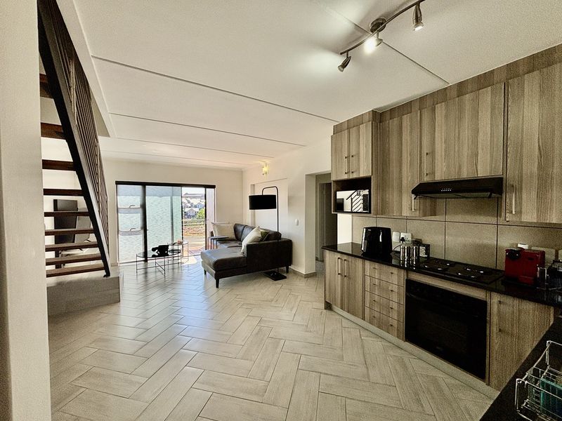 Modern open-plan living area featuring a contemporary kitchen with granite countertops, herringbone tiled floors, and a timber staircase leading to the upper level.