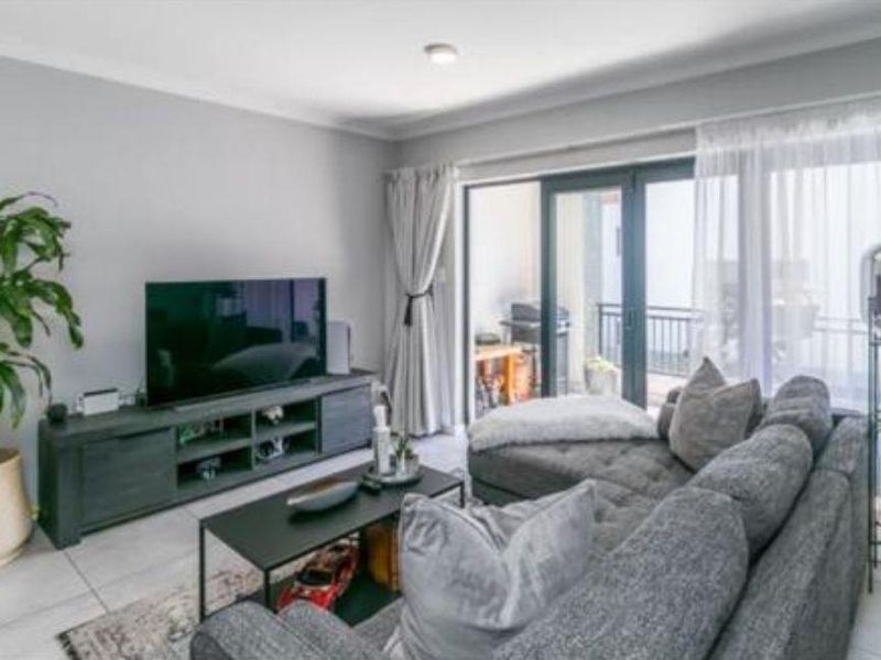 A well-maintained living room featuring neutral grey walls, tiled flooring, and large sliding glass doors providing access to an outdoor balcony area.
