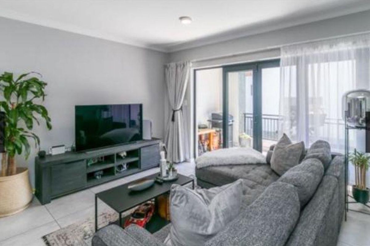 A well-maintained living room featuring neutral grey walls, tiled flooring, and large sliding glass doors providing access to an outdoor balcony area.