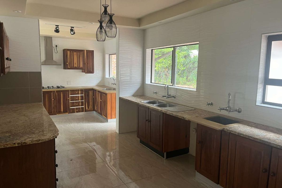 Spacious kitchen featuring wooden cabinetry, granite countertops, double sink, and a built-in gas hob with extractor fan.