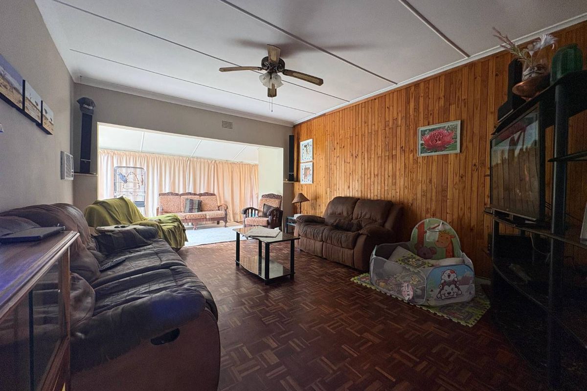 Spacious living room featuring parquet flooring, wood-paneled accent wall, and a ceiling fan, with an open transition to an adjoining sunroom area.