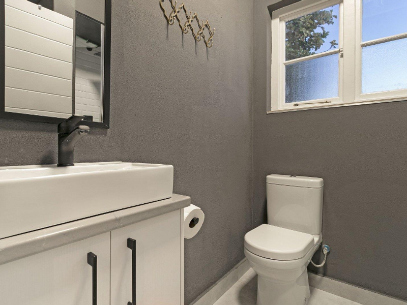 A modern bathroom featuring a white vanity cabinet with a vessel sink, a contemporary faucet, and a standard toilet against dark grey walls.