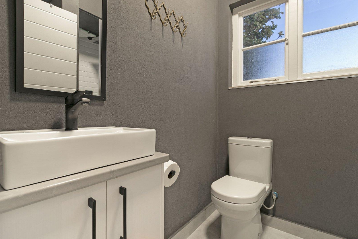 A modern bathroom featuring a white vanity cabinet with a vessel sink, a contemporary faucet, and a standard toilet against dark grey walls.