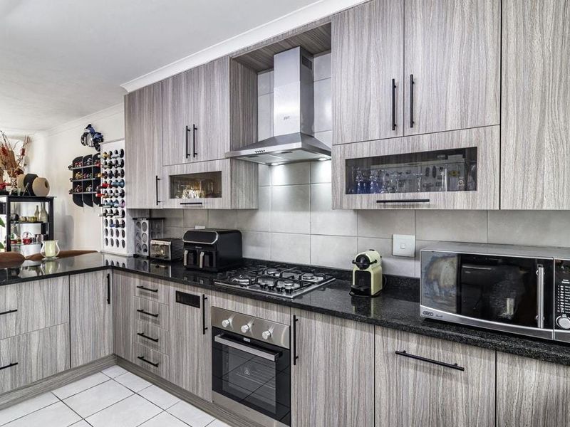 Modern kitchen featuring wood-grain cabinetry, granite countertops, a gas hob, built-in oven, and stainless steel extractor fan with tiled flooring.