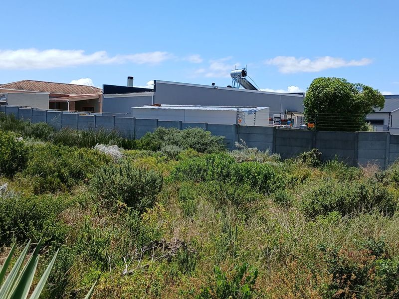 A view of the rear boundary of the vacant residential plot, featuring a precast concrete wall with electric fencing and neighbouring property structures.