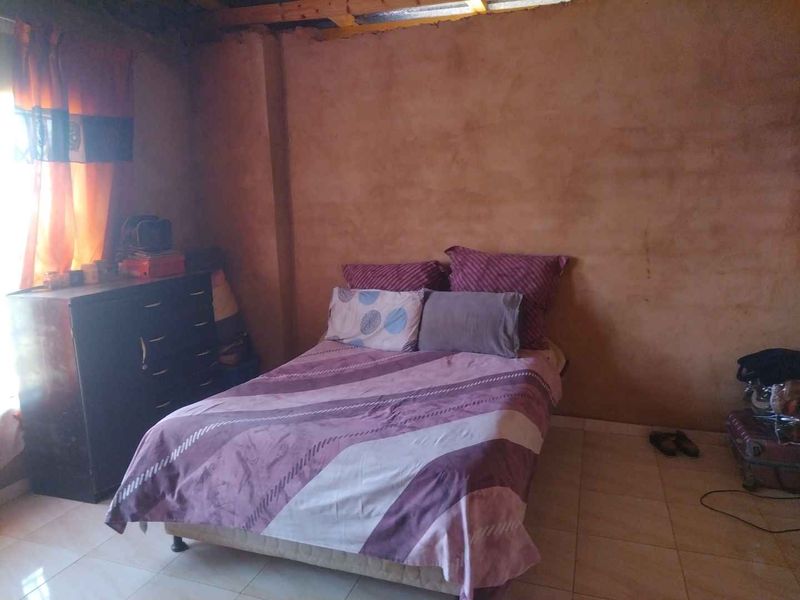 A bedroom featuring tiled flooring and exposed timber ceiling beams, currently requiring wall finishing and ceiling completion to improve the overall aesthetic.