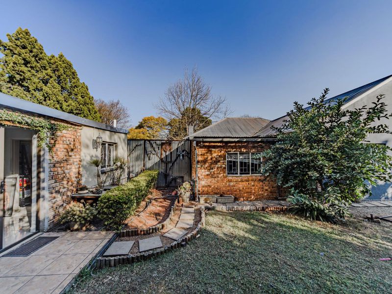 Rear view of the property featuring a brick facade, corrugated metal roof, paved walkway, and a small garden area.
