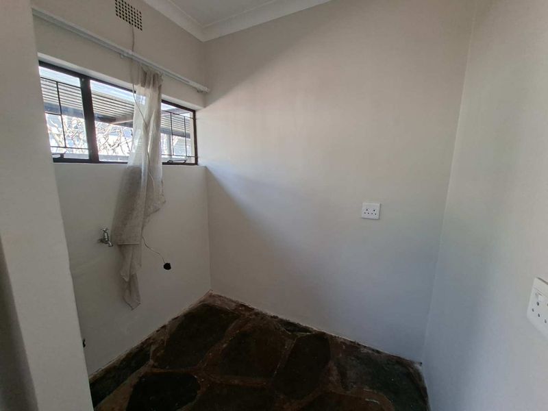 A functional laundry area featuring stone flooring, plumbing connections, and electrical outlets, ready for appliance installation.