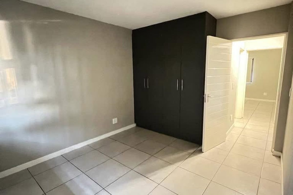 A clean, empty bedroom featuring neutral tiled flooring, dark built-in cupboards, and a simple ceiling light fixture.