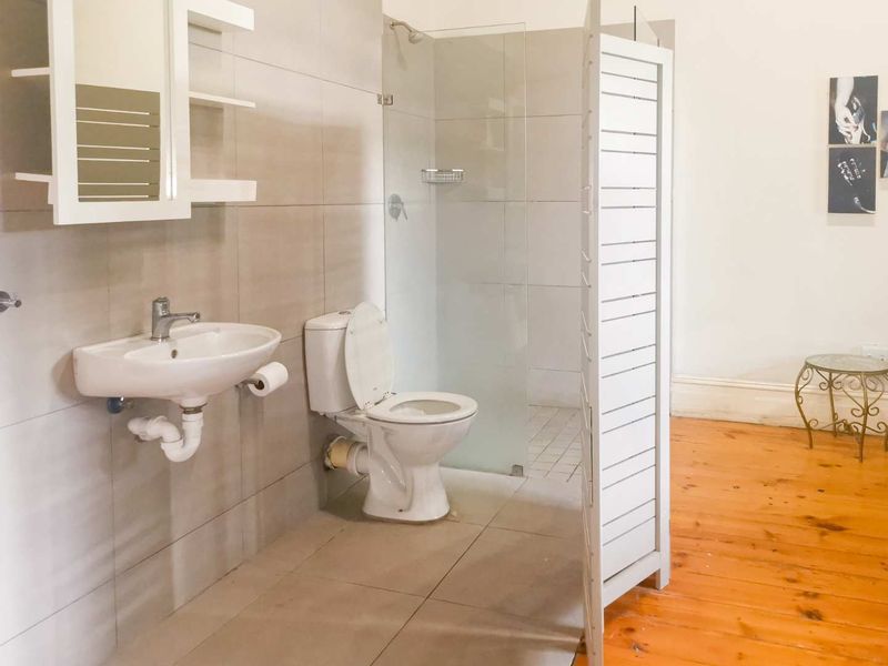 A functional bathroom featuring a wall-mounted basin, toilet, and a glass-enclosed shower area with neutral wall tiling and wooden flooring.