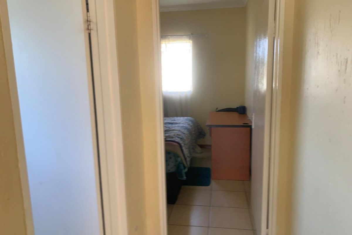 A view through a doorway into a bedroom featuring tiled flooring and a window, showing basic finishes and a compact layout.