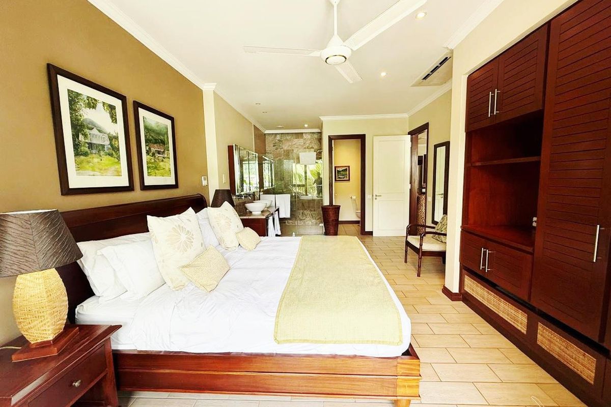 Spacious bedroom featuring built-in wooden cabinetry, tiled flooring, a ceiling fan, and an integrated en-suite bathroom with a stone-tiled shower area.