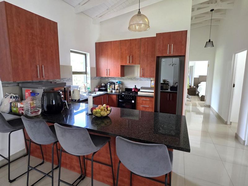 Modern kitchen featuring dark granite countertops, wooden cabinetry, built-in appliances, and a breakfast bar, set under a high vaulted ceiling with tiled flooring.