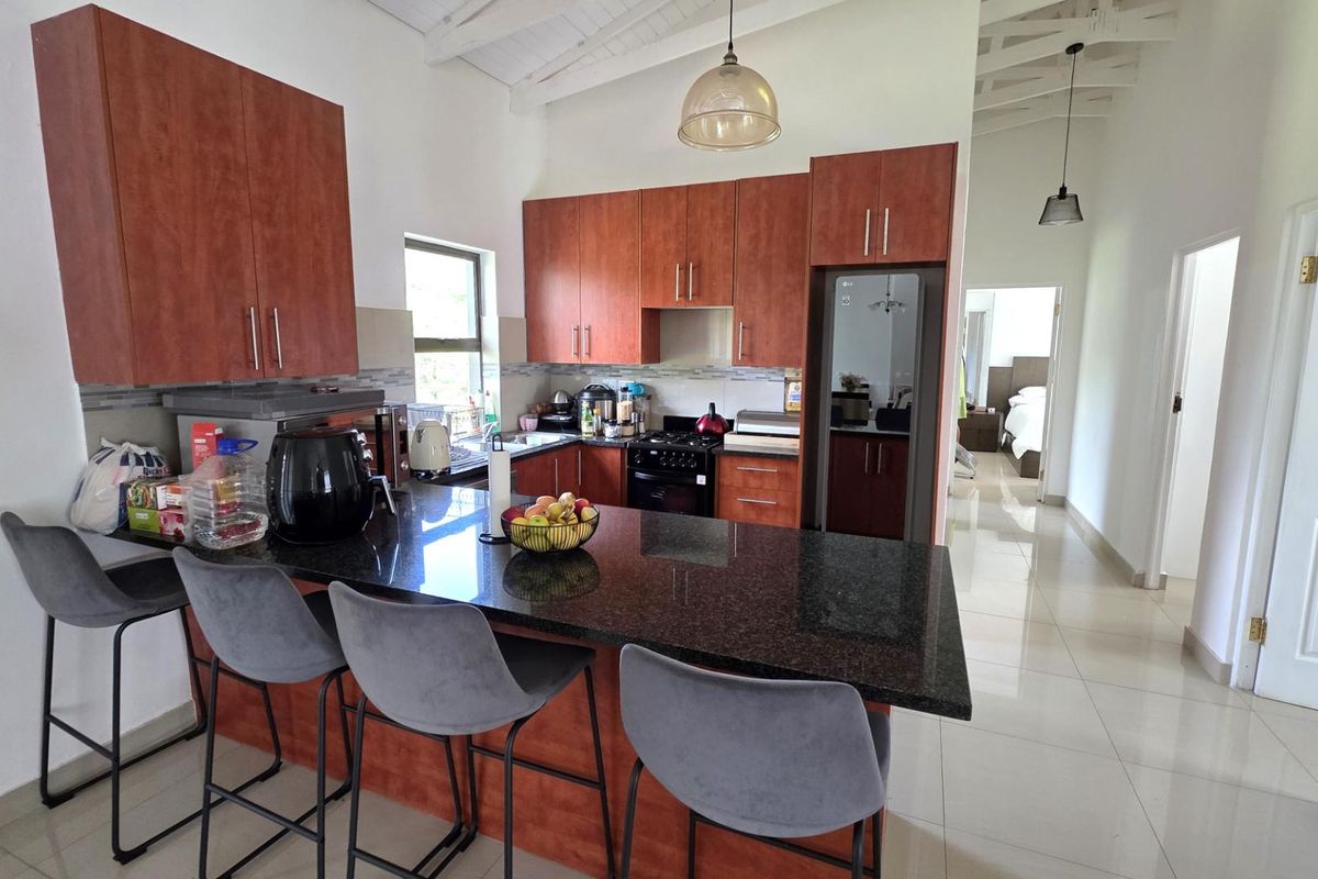 Modern kitchen featuring dark granite countertops, wooden cabinetry, built-in appliances, and a breakfast bar, set under a high vaulted ceiling with tiled flooring.