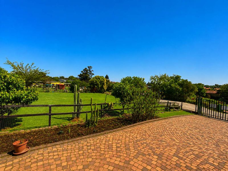 A well-maintained garden area featuring a paved driveway, secure metal fencing, and a spacious lawn on this small holding property.