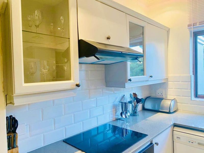 A well-maintained kitchen featuring white cabinetry, subway tile backsplash, stone countertops, and a built-in induction hob with an extractor fan.