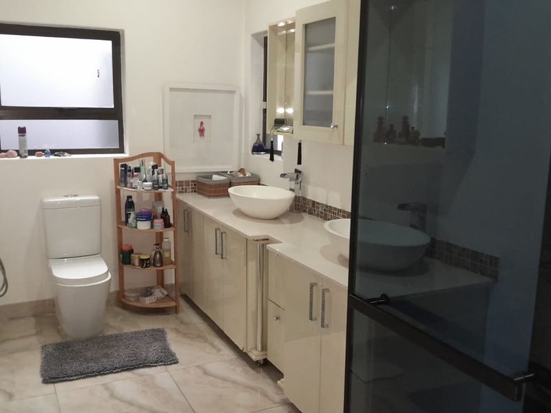 A modern bathroom featuring a dual vanity with vessel sinks, built-in cabinetry, tiled flooring, and a glass-enclosed shower.