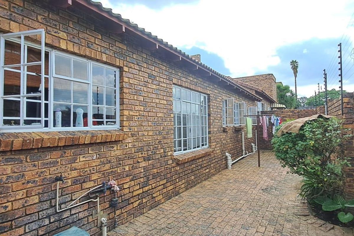 A side exterior view of the townhouse featuring face-brick walls, paved walkway, and perimeter security fencing.