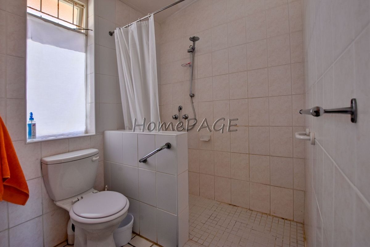 A functional bathroom featuring a tiled shower area with grab rails, a standard toilet, and neutral wall tiling.