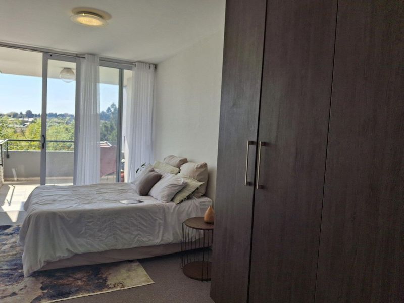 A well-lit bedroom featuring a large built-in wardrobe and sliding glass doors that open onto a private balcony with scenic views.