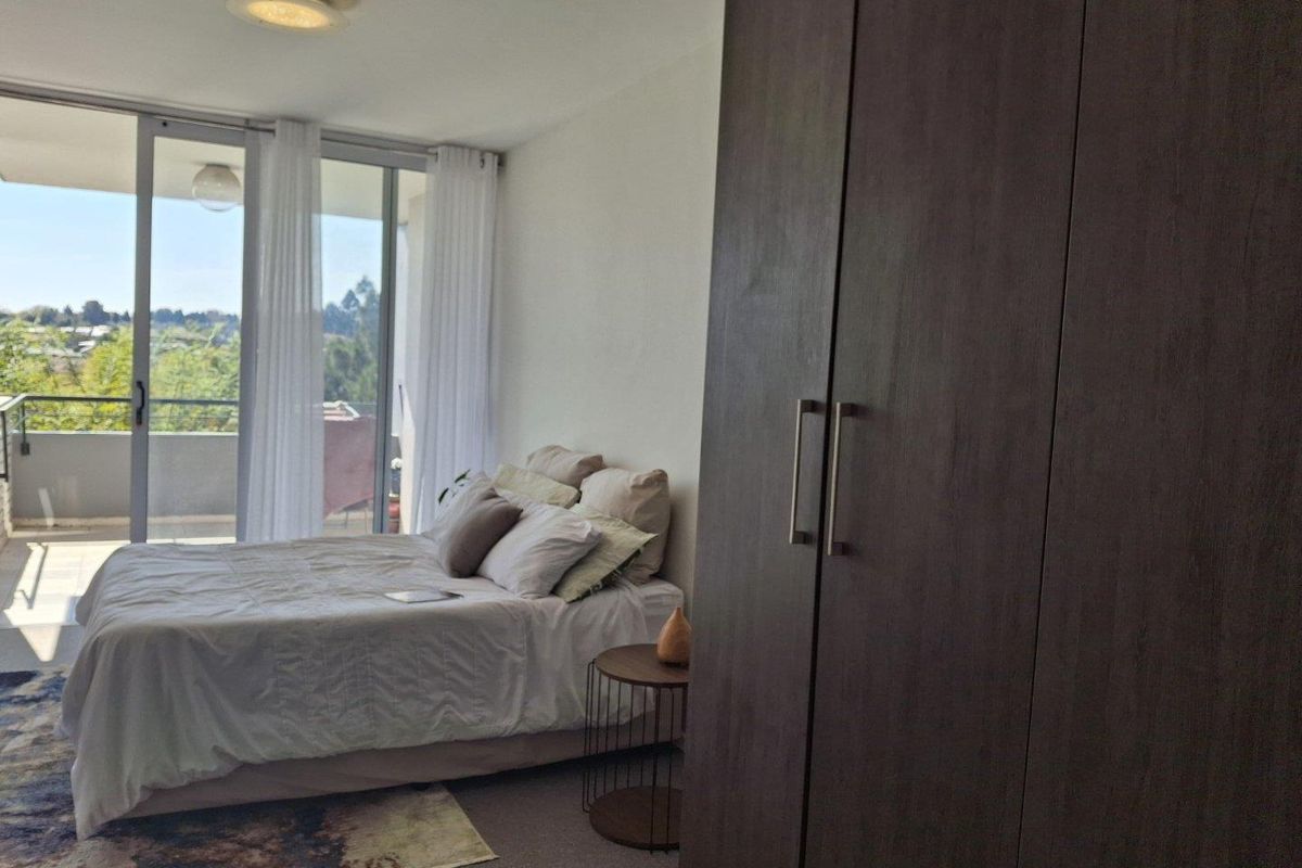 A well-lit bedroom featuring a large built-in wardrobe and sliding glass doors that open onto a private balcony with scenic views.