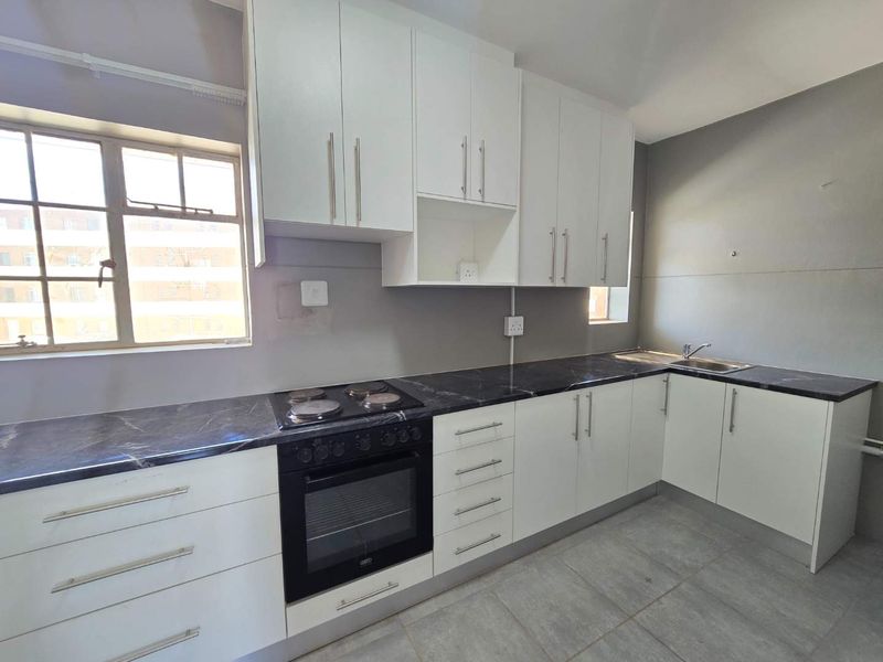 A clean, modern kitchen featuring white cabinetry, dark marble-effect countertops, built-in oven and hob, and tiled flooring.