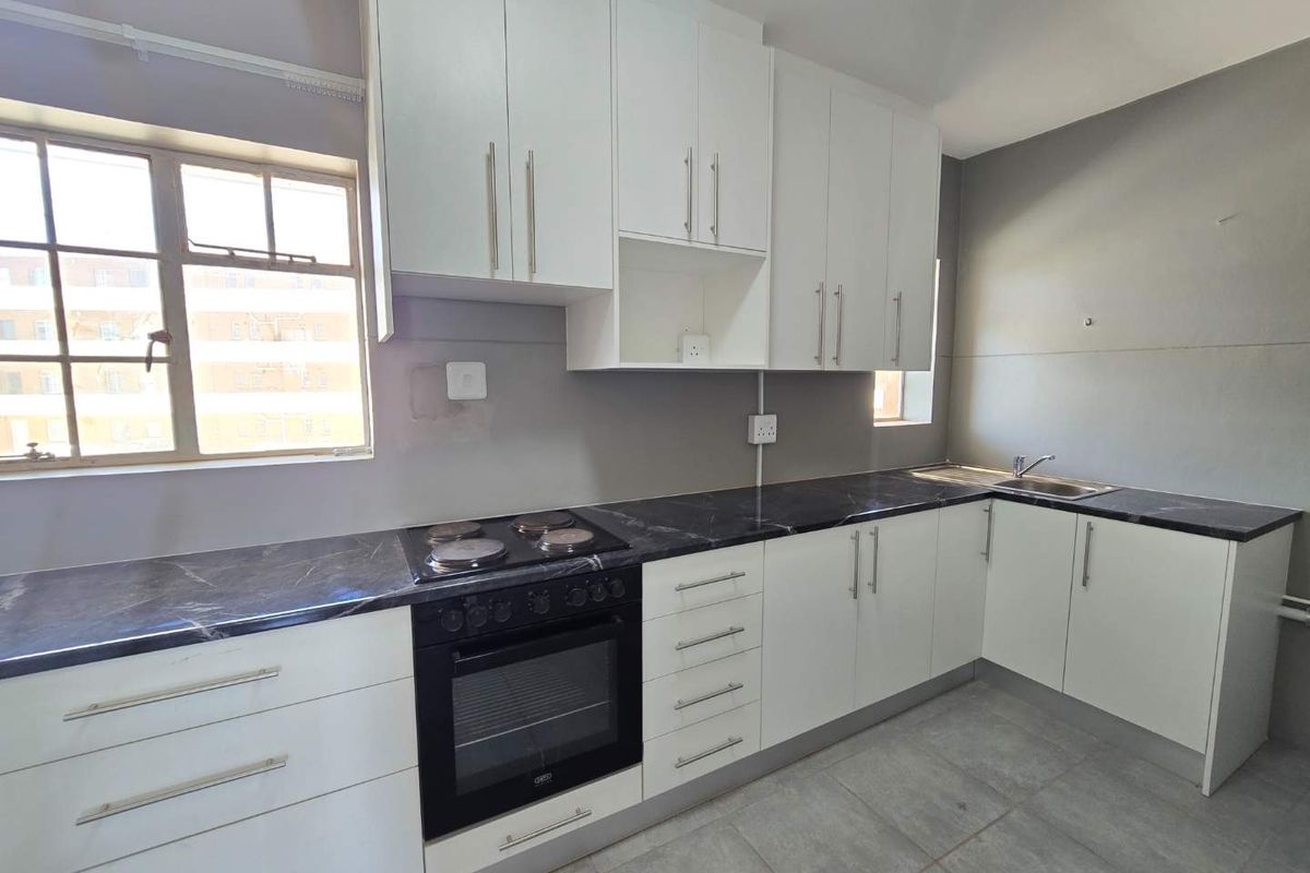 A clean, modern kitchen featuring white cabinetry, dark marble-effect countertops, built-in oven and hob, and tiled flooring.