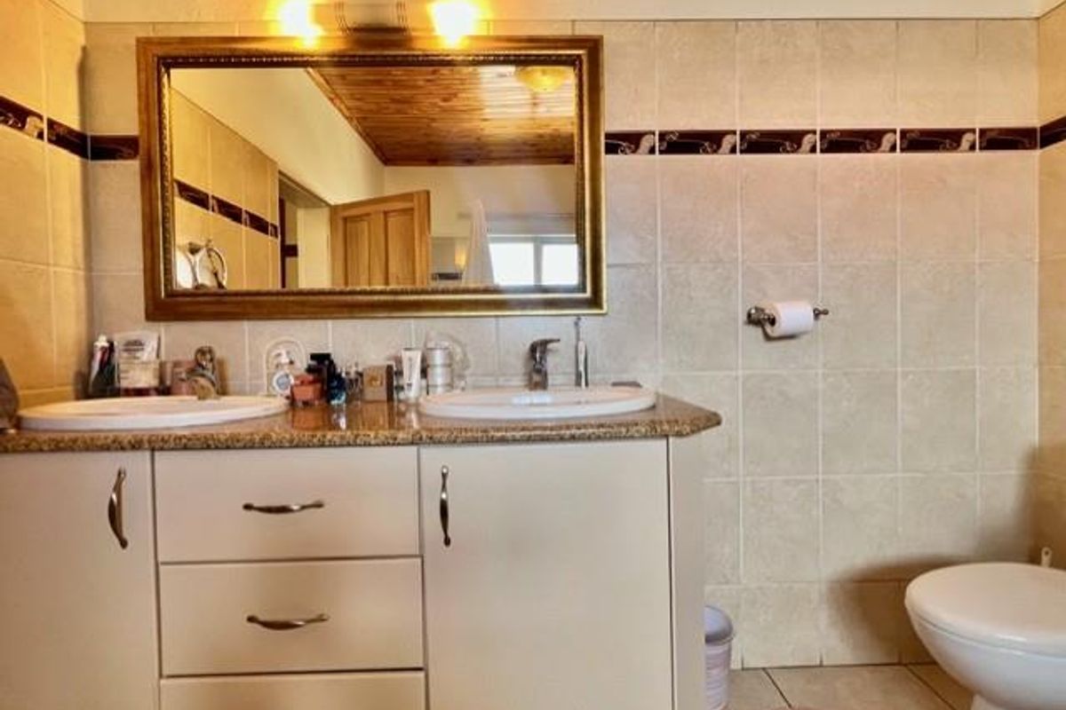 A functional bathroom vanity area featuring dual basins, granite-style countertops, and a large framed mirror against tiled walls.